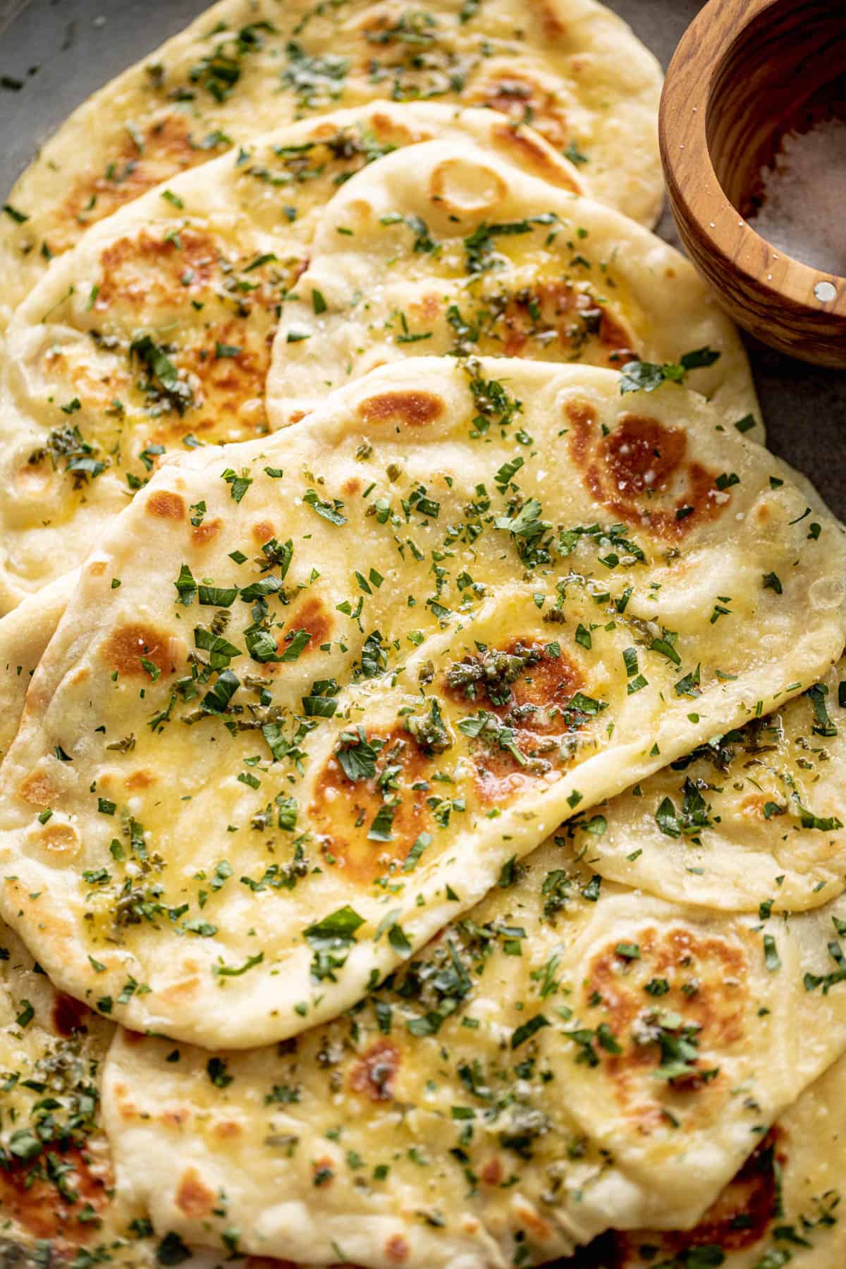 Stack of garlic naan bread with herbs on a stone surface