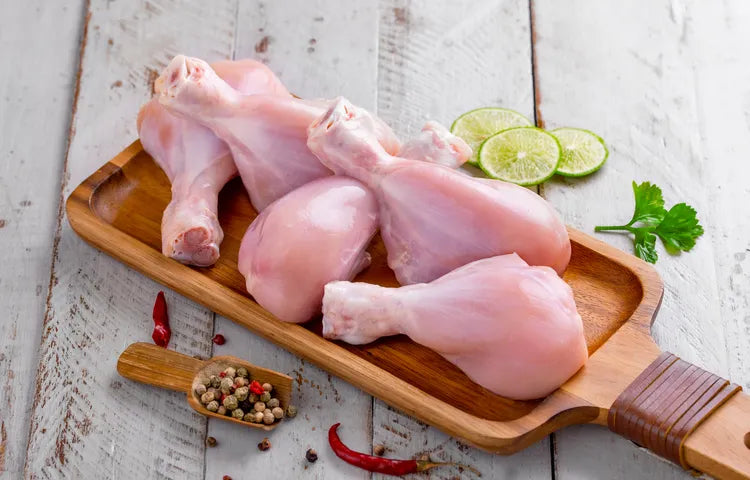 Fresh zabiha halal chicken drumsticks on a wooden cutting board with a sprig of lime and a spice mix, placed on a wooden surface.