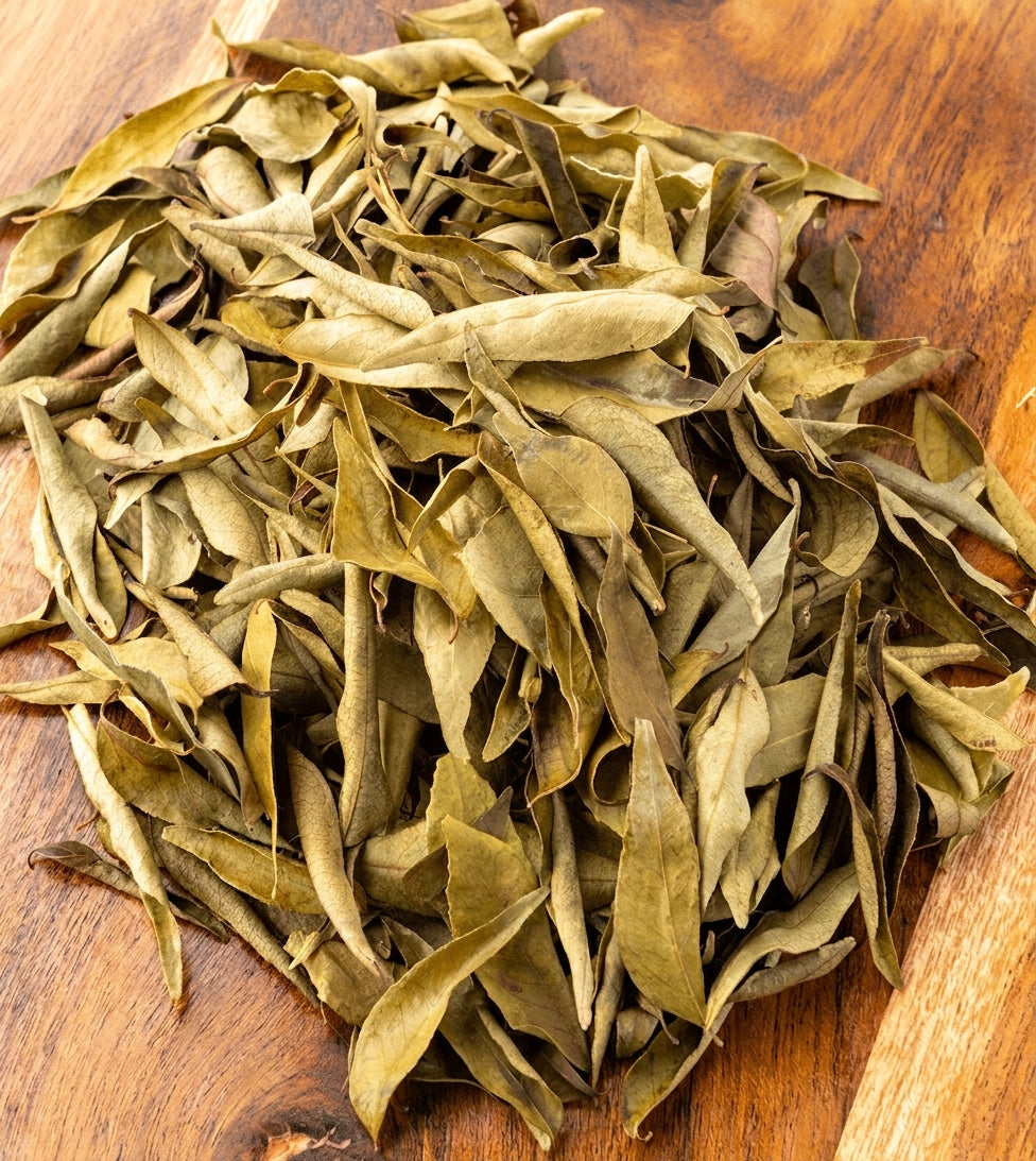 A pile of dried, curled tea leaves in shades of olive green and brown, arranged on a wooden surface.
