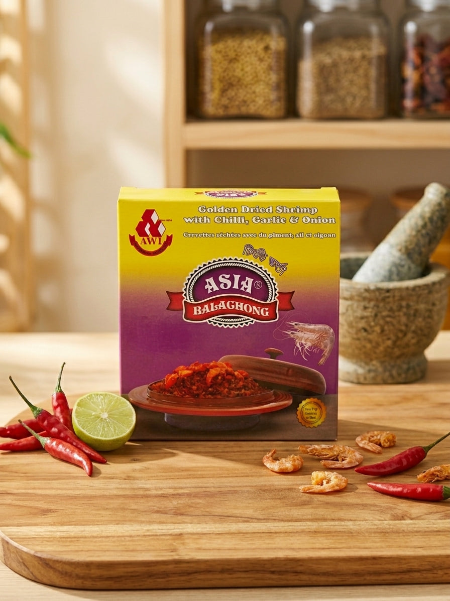 A box of Asia Balachong Golden Dried Shrimp with Chili, Garlic & Onion seasoning mix, styled on a wooden cutting board with red chilies, a lime wedge, and dried shrimp, with a blurred kitchen spice jar background.