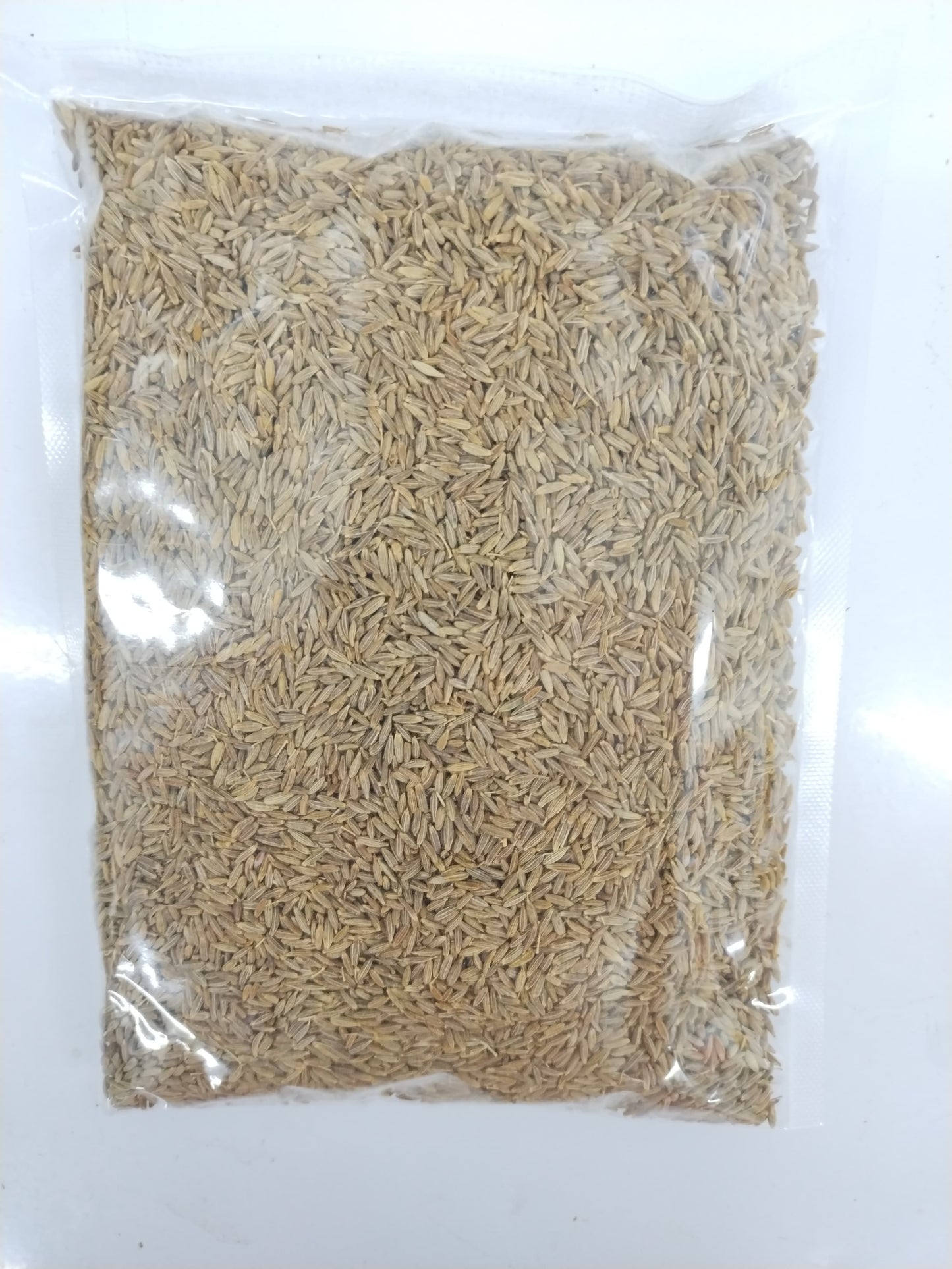 A clear plastic bag filled with light tan to beige dried grains or seeds, photographed against a plain white background.