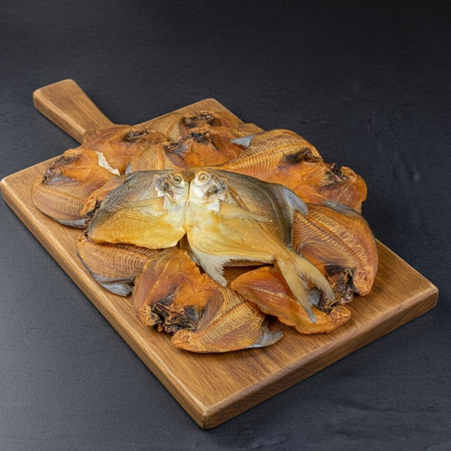 Dried silver pomfret fish on a wooden cutting board against a dark background