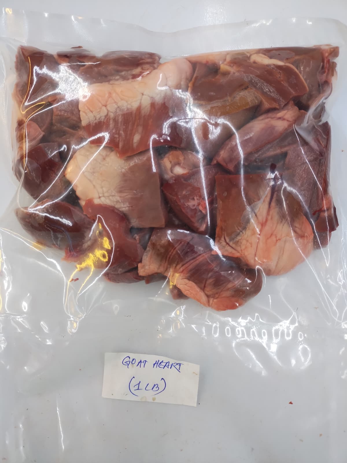 A vacuum-sealed clear plastic bag containing cut raw goat meat, with a small handwritten label reading 'GOAT Heart (1 LB)' at the bottom.