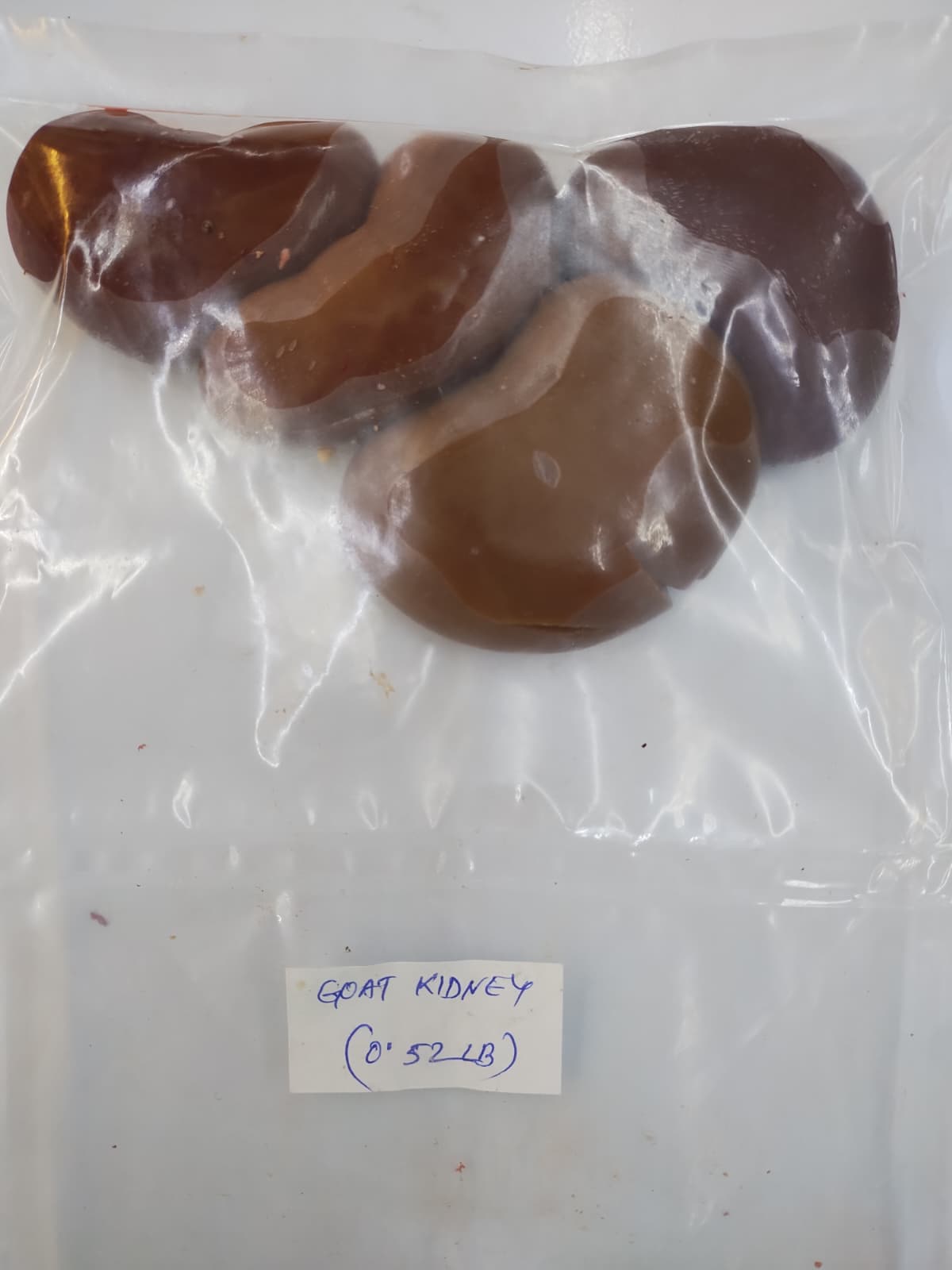 Four brown goat kidneys in a clear plastic bag with a handwritten label reading 'GOAT KIDNEYS (0'52 LB)'.