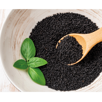 Black seeds in a bowl with a wooden spoon and basil leaves on a light background