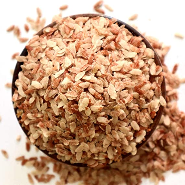 Brown rice in a bowl with scattered grains on a white background