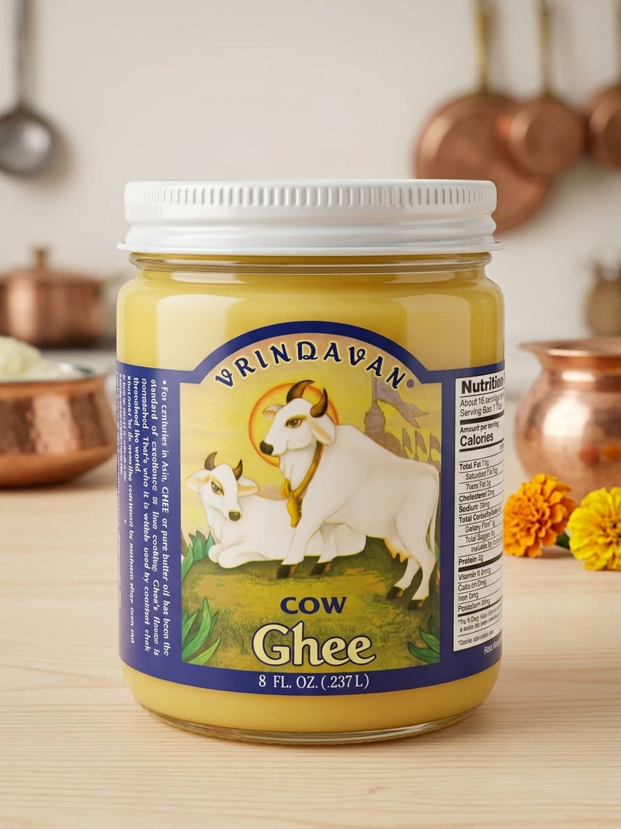 A jar of Vrndavan Cow Ghee on a light wooden table with copper pots blurred in the background.