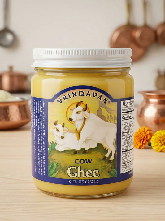 A jar of Vrndavan Cow Ghee on a light wooden table with copper pots blurred in the background.