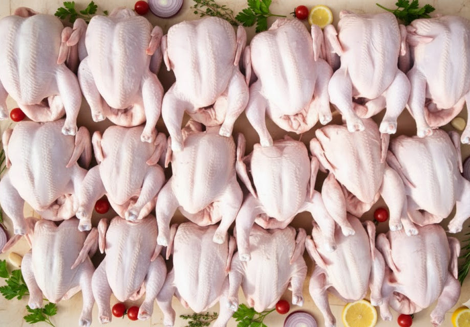Multiple raw chickens arranged on a surface with garnishes.