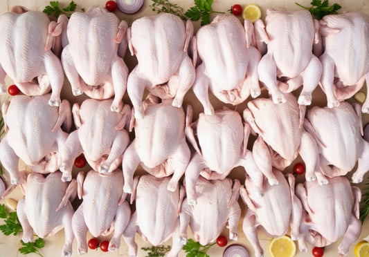 Multiple raw chickens arranged on a surface with garnishes.