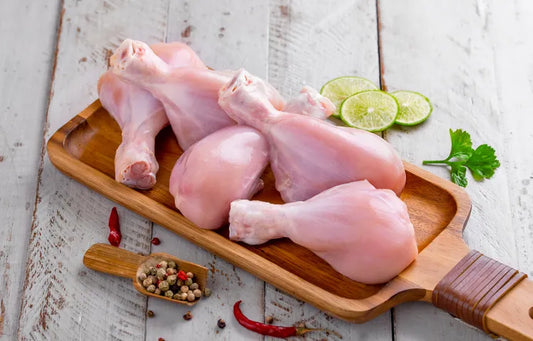 Fresh zabiha halal chicken drumsticks on a wooden cutting board with a sprig of lime and a spice mix, placed on a wooden surface.
