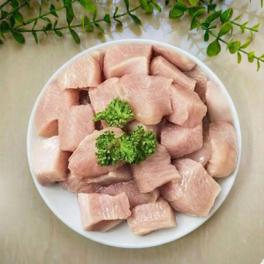 Raw zabiha halal chicken tikka cube pieces from boneless breast pieces on a white plate with green leaves in the background